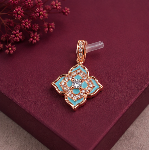 A rose gold flower-shaped pendant with turquoise enamel and clear rhinestones, displayed on a dark burgundy box with small pink flowers in the corner.