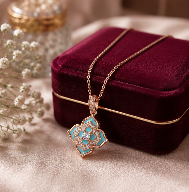 A rose gold pendant necklace with turquoise enamel and clear stones, draped over a deep burgundy velvet jewelry box on a beige fabric surface.