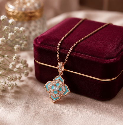 A rose gold pendant necklace with turquoise enamel and clear stones, draped over a deep burgundy velvet jewelry box on a beige fabric surface.